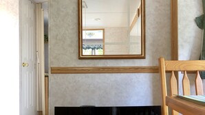 Een kamer met een open haard, een spiegel aan de muur, een houten stoel en een deur die naar een andere kamer leidt.