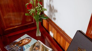 A wooden table with a magazine, a vase with flowers, and a plate with apples.