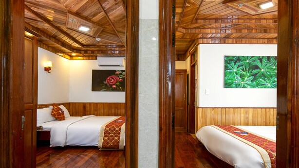 A room with wooden floors and walls, two beds with white bedding, a wall-mounted air conditioner, and a framed picture of a plant.