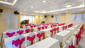 A banquet hall with rows of tables and chairs, each with a white tablecloth and chairs adorned with pink bows.