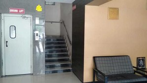 A reception area with a ground lift door, a staircase, and a checkered bench. - i-ROOMZ Hoysala Residency (Ballari)
