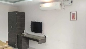 A room with a dark wood wardrobe, a mounted flat-screen TV, and a built-in bench with a coffee machine. - i-ROOMZ Hoysala Residency (Ballari)