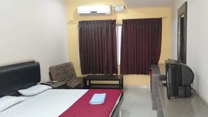 A hotel room with a bed, a desk, a chair, a television, and an air conditioning unit. - i-ROOMZ Hoysala Residency (Ballari)