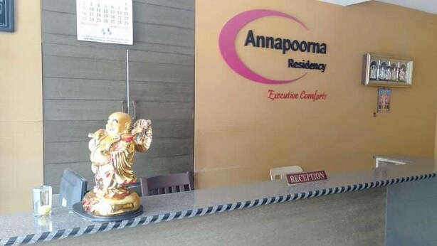 A reception desk with a statue, a calendar, and a sign indicating the reception area. - i-ROOMZ Hoysala Residency (Ballari)