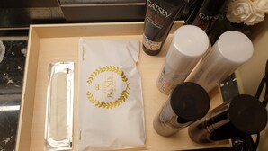 A tray with a comb, a white towel, and toiletries including a black bottle, a white bottle, and a tube.