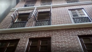 A multi-story building with brick walls and multiple windows, some with metal grilles. - Heritage De Patan (Lalitpur)