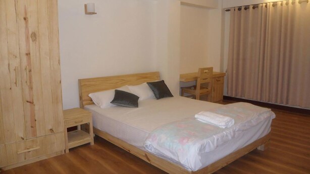A bedroom with a wooden bed, a nightstand, a wooden wardrobe, and a desk with a chair. - Heritage De Patan (Lalitpur)