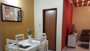 Un coin repas avec une table et des chaises blanches, un vase de fleurs et un tableau encadré au mur.