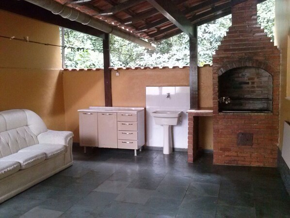 A covered outdoor area with a brick oven, a white sofa, a cabinet, and a sink.
