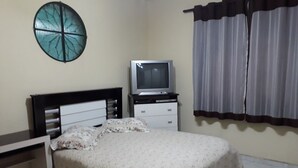 Une chambre à coucher avec un lit, un téléviseur posé sur un meuble, une table de chevet, une fenêtre circulaire fixée au mur et une fenêtre avec des rideaux.