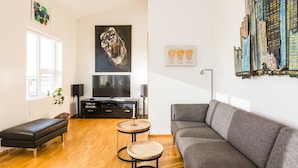 Ein modernes Wohnzimmer mit grauem Sofa, einer schwarzen Bank, einem Holztisch und einem Flachbildfernseher.