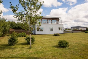 A modern two-story house with a flat roof, large windows, and a well-maintained lawn.