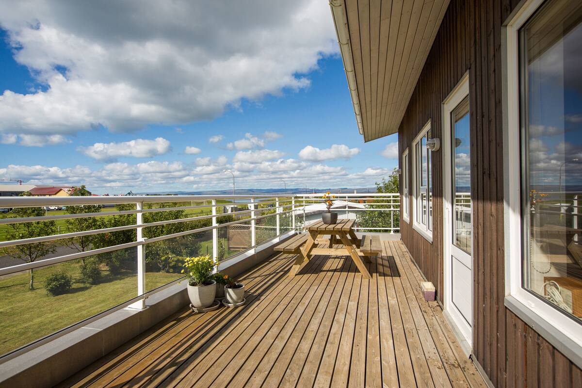 A wooden deck with a table and chairs, potted plants, and a view of the landscape.