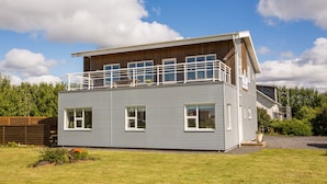 Ein modernes Haus mit zwei Etagen, einem Balkon, großen Fenstern und einer Holzterrasse.