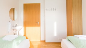 Ein Schlafzimmer mit zwei Betten, einem Holzschrank, einem Spiegel und einem weißen Waschbecken.