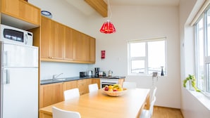 Eine moderne Küche mit Holzausstattung, einem weißen Kühlschrank, einem Esstisch mit Stühlen, einer Obstschale und einer roten Pendelleuchte.