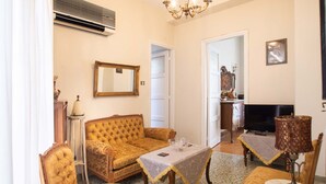 A living room with a sofa, armchairs, a coffee table, a TV, and a chandelier. - Classic Central Athinian Apartment (Athens)