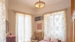 A bedroom with a bed, a chair, a radiator, and a window with curtains. - Classic Central Athinian Apartment (Athens)