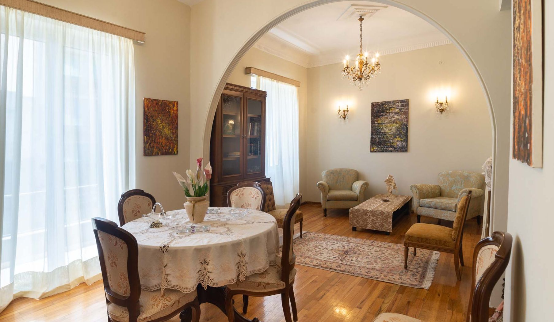 A dining area with a round table, chairs, a chandelier, and artwork on the walls.