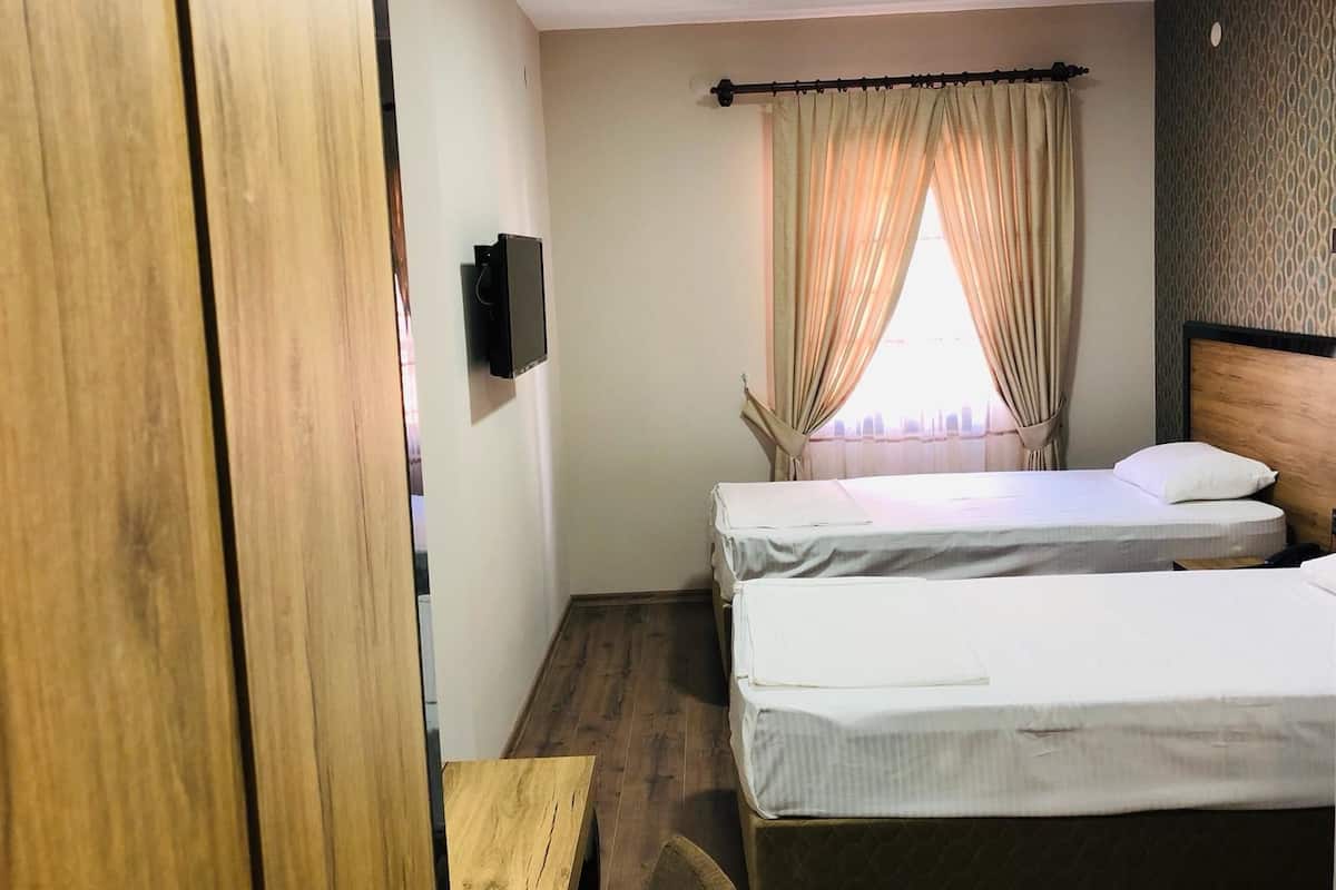 Habitación de hotel con dos camas individuales, un armario de madera, una mesita pequeña y un televisor fijado a la pared.