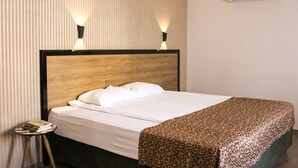 Een net opgemaakt bed met een houten hoofdbord, twee bedlampjes en een geborduurde plaid.