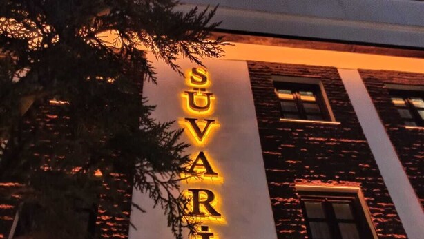 Een hotelschild met de naam 'SUVARI HOTEL' verlicht in heldere letters.