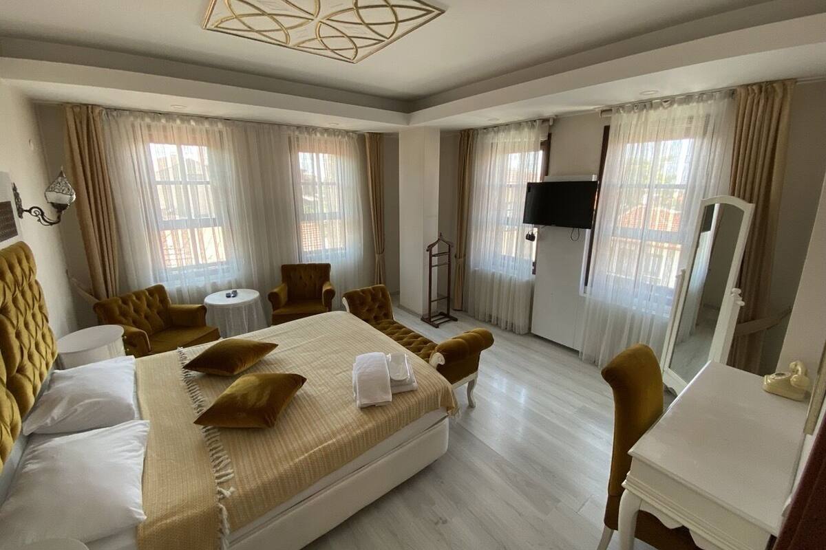 Ein Hotelzimmer mit einem großen Bett, zwei Sesseln, einem kleinen runden Tisch, einem Fernseher und einem Schreibtisch mit Telefon.