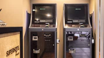 Dos quioscos de autoservicio con pantallas y lectores de tarjetas, una puerta con manija, y un letrero que dice "Superhotel".