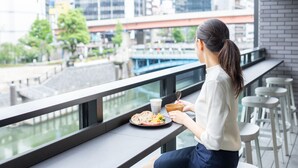 A person sitting at a table with a meal, overlooking a river and cityscape.