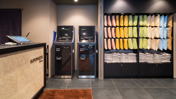 A hotel reception area with a digital kiosk, a self-service machine, and a wall displaying neatly folded towels.