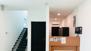 A reception area with a wooden desk, a black door, a staircase, and a wall-mounted air conditioner. - Luna Stay by Yolodge (Lunas)
