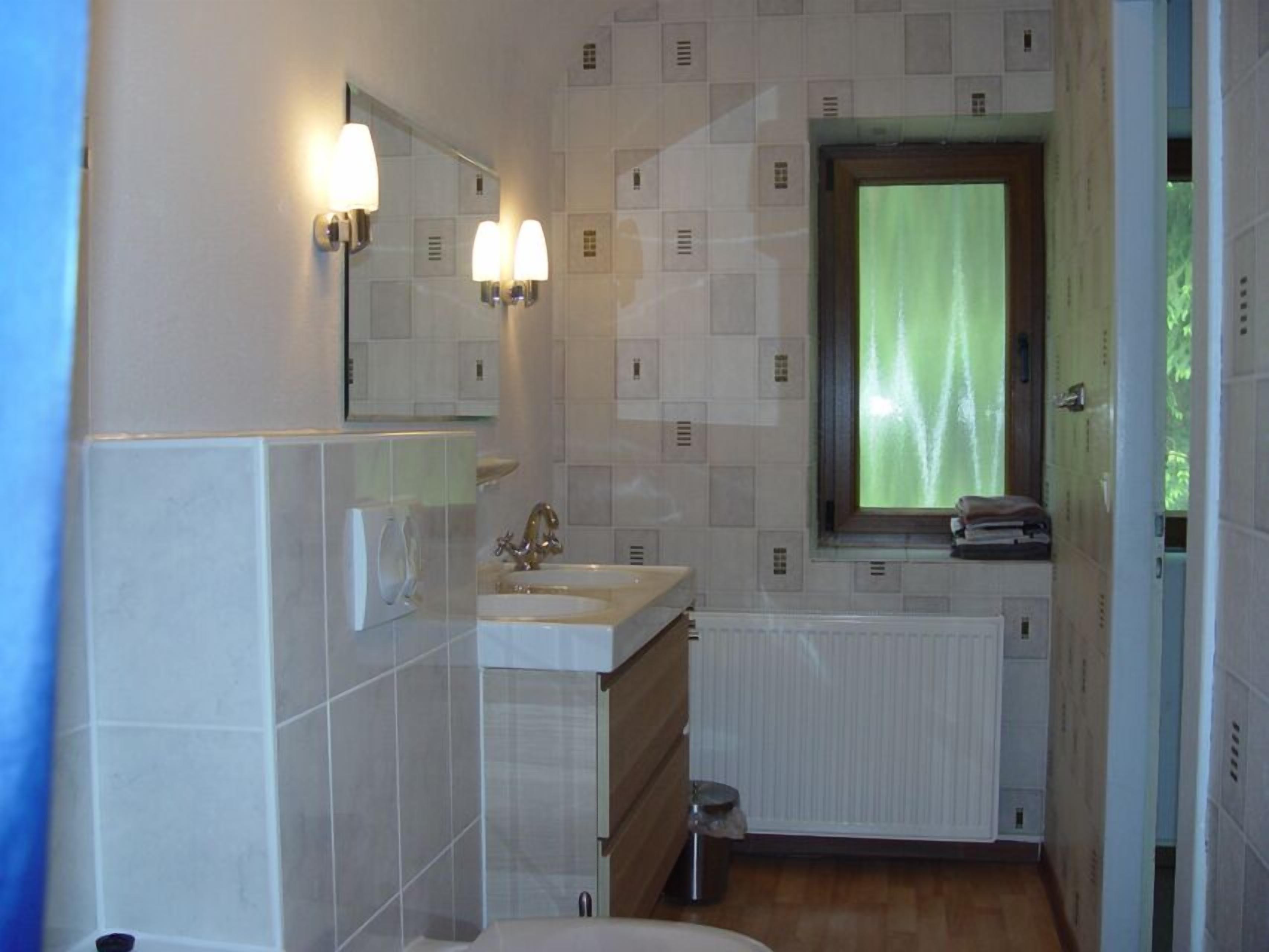 Une salle de bain avec deux lavabos, un miroir et une fenêtre ornée d’un rideau vert.