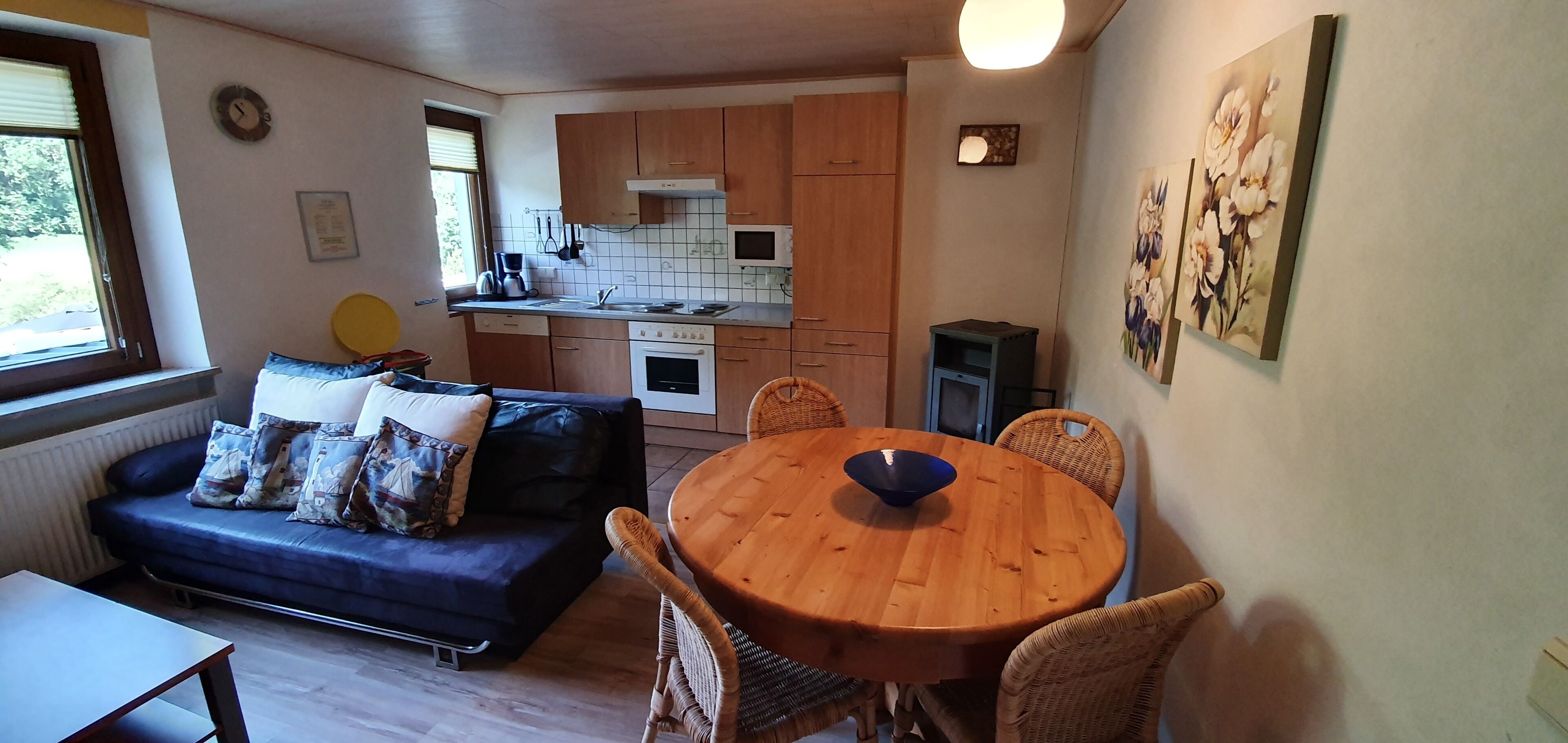 A compact living space with a sofa, dining table, kitchen area, and artwork on the walls.
