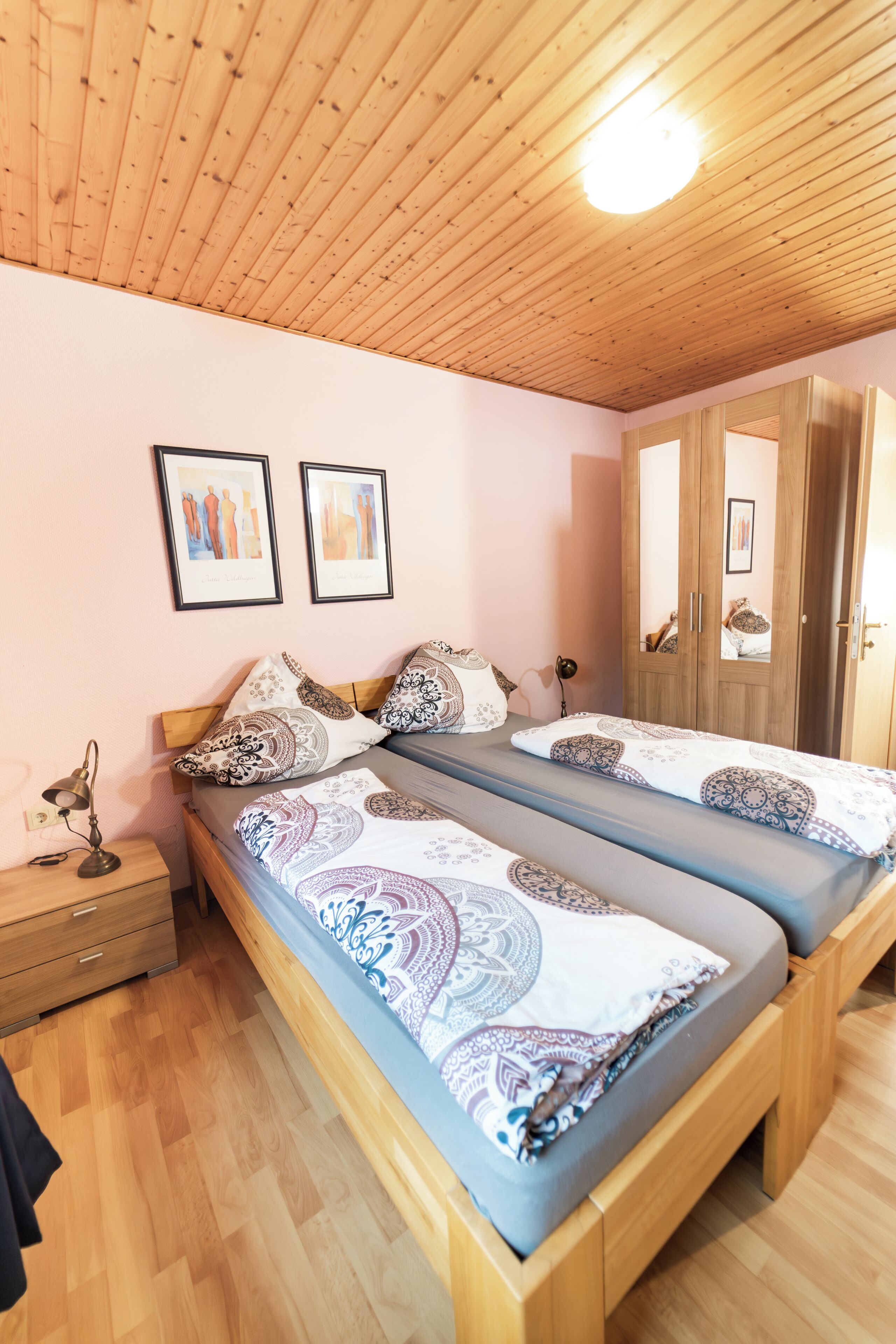 Una habitación con dos camas, suelo de madera, una lámpara en el techo y un armario.