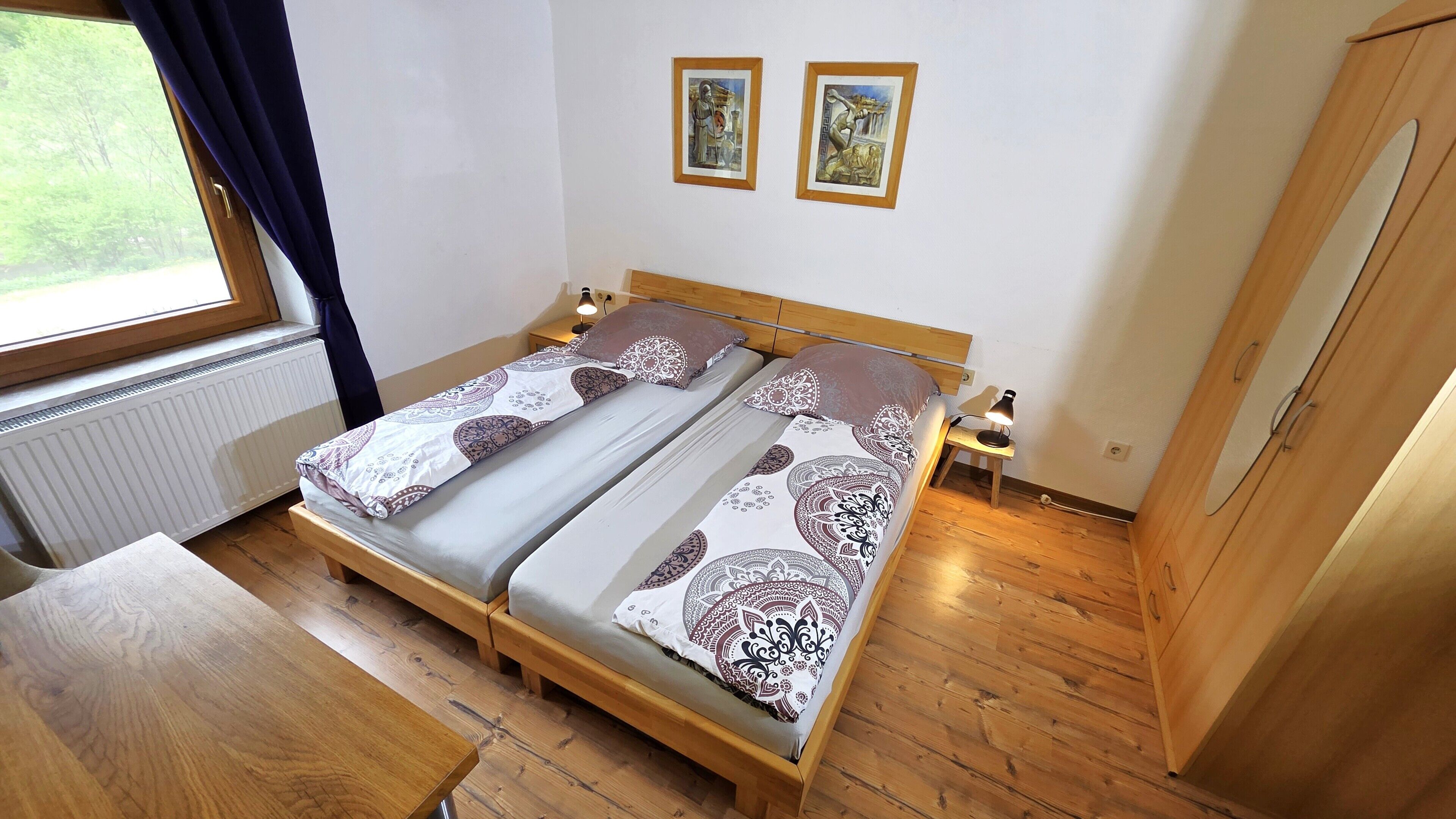 Una cama doble con ropa de cama estampada, una mesita de noche con lámpara y dos cuadros en la pared.