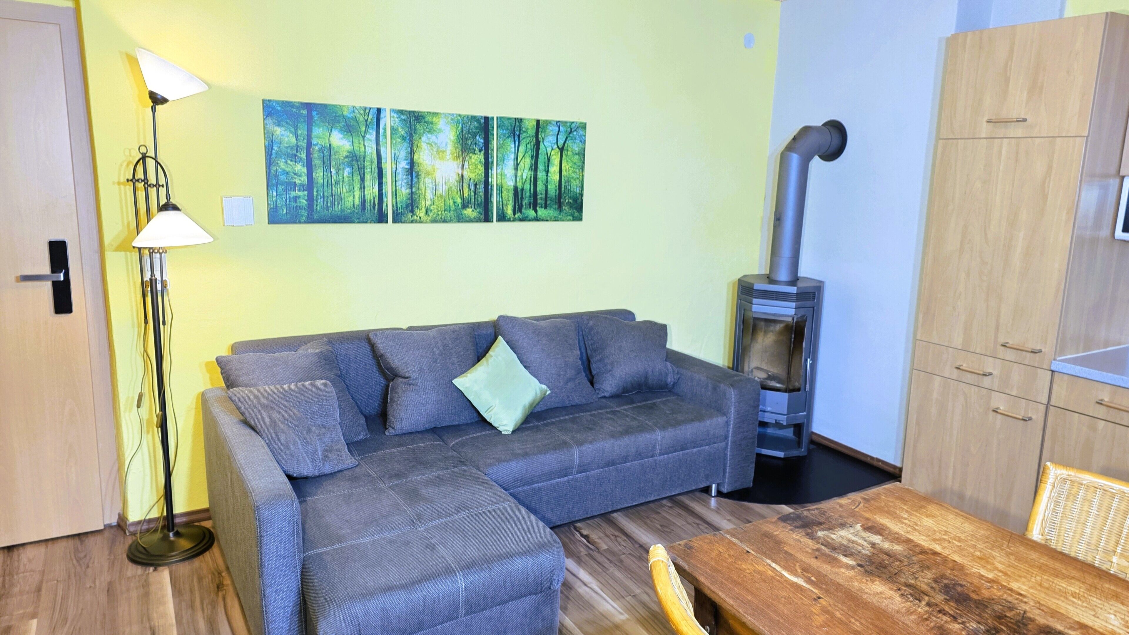 Une pièce comprenant un canapé, une lampe sur pied, une table en bois, un radiateur fixé au mur et un meuble de rangement.