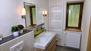 Un baño con dos lavamanos, un espejo, un radiador y una ventana con persianas.
