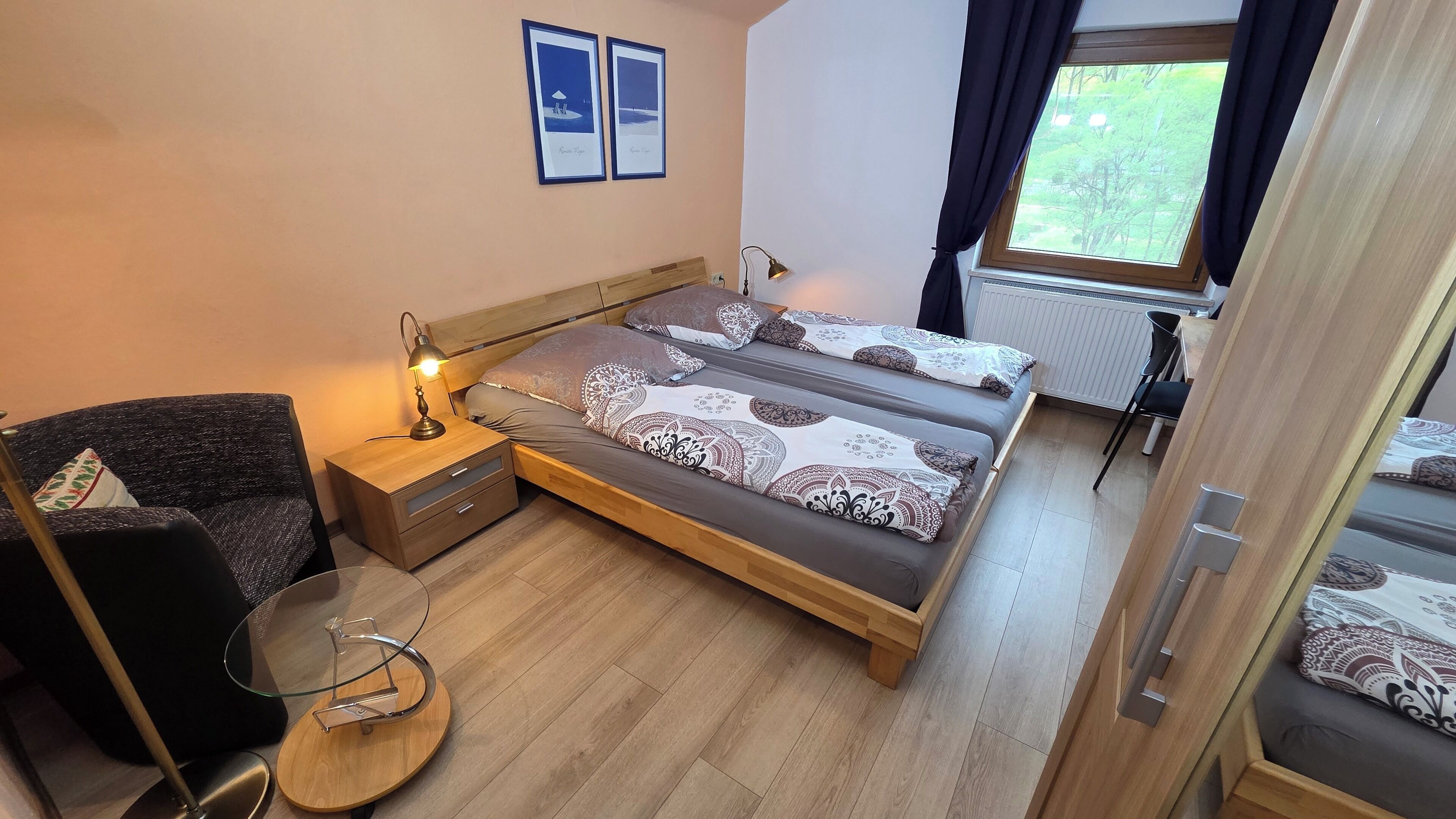 A bedroom with a bed, bedside table, lamp, chair, and a window with curtains.