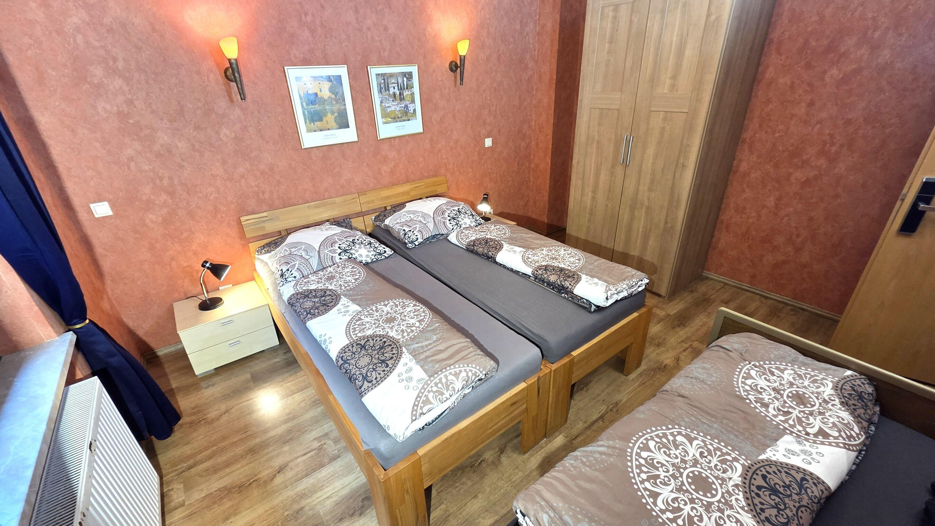 A double bed with patterned bedding, a bedside table with a lamp, a wardrobe, and two wall-mounted light fixtures.