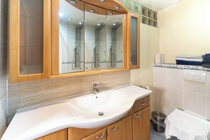 Un baño con un lavamanos blanco, armarios de madera, un espejo y una pared con azulejos.