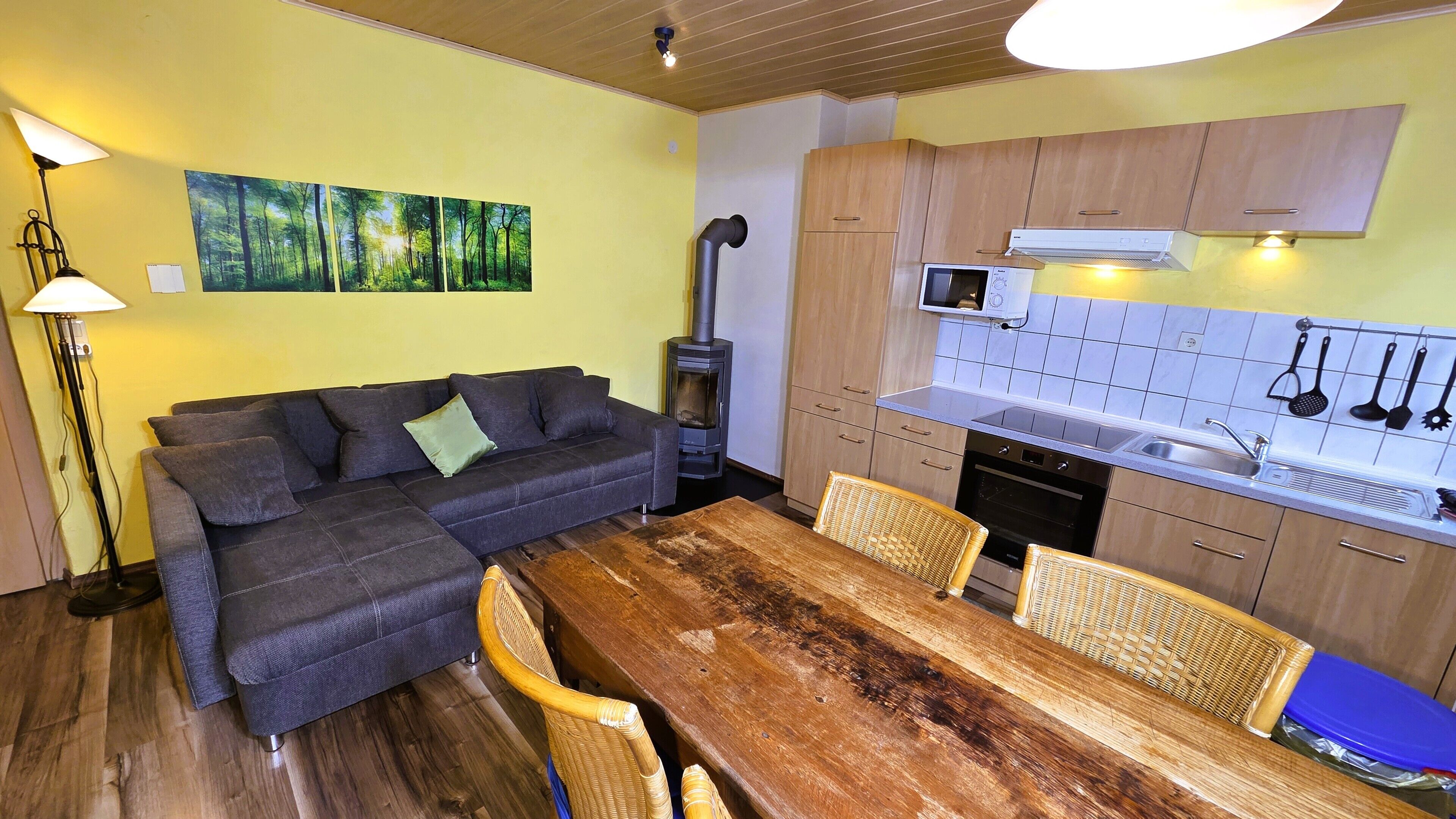 A compact living space with a sofa, dining table, kitchen area, and a large painting on the wall.