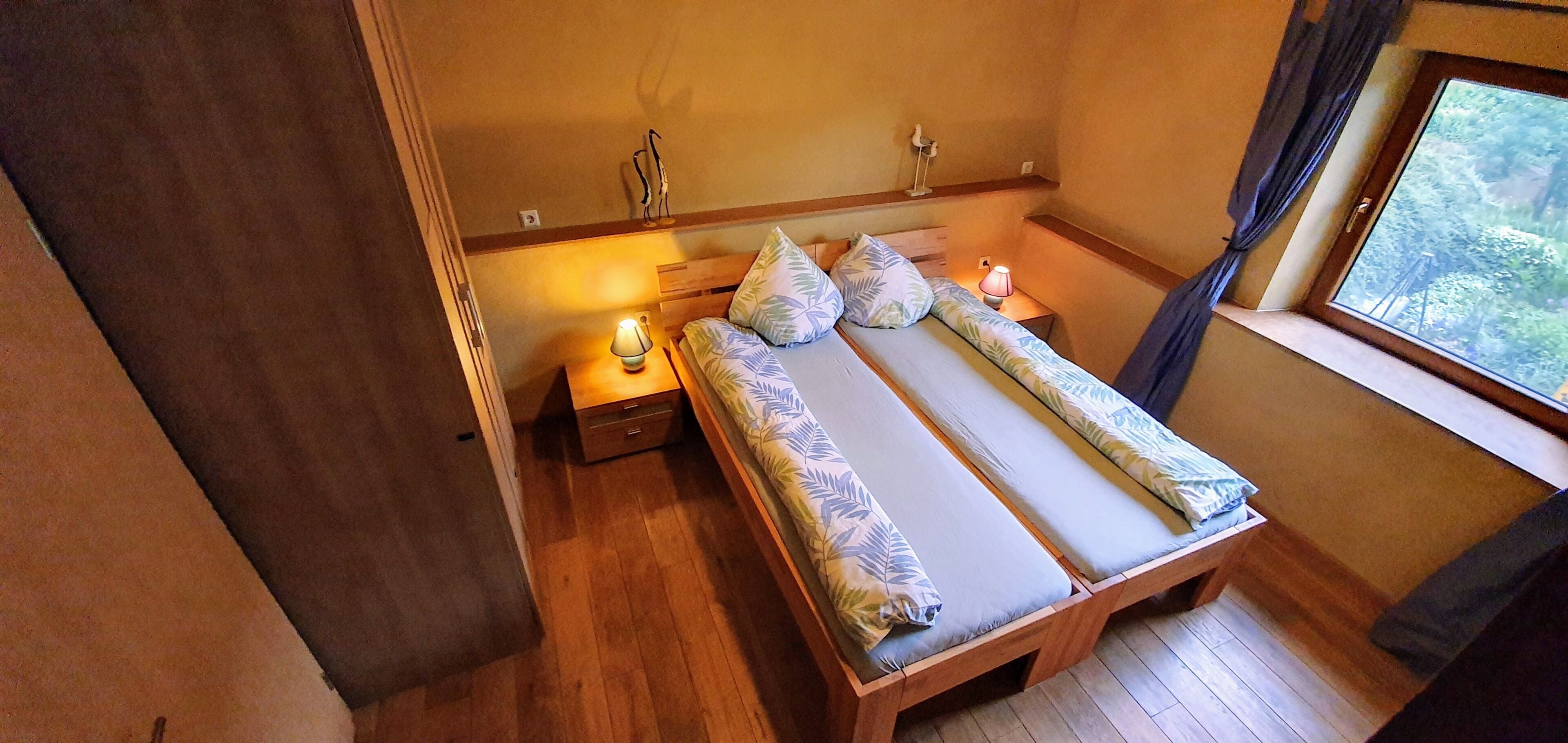 A bedroom with a bed, bedside table, lamp, and a window with a view.