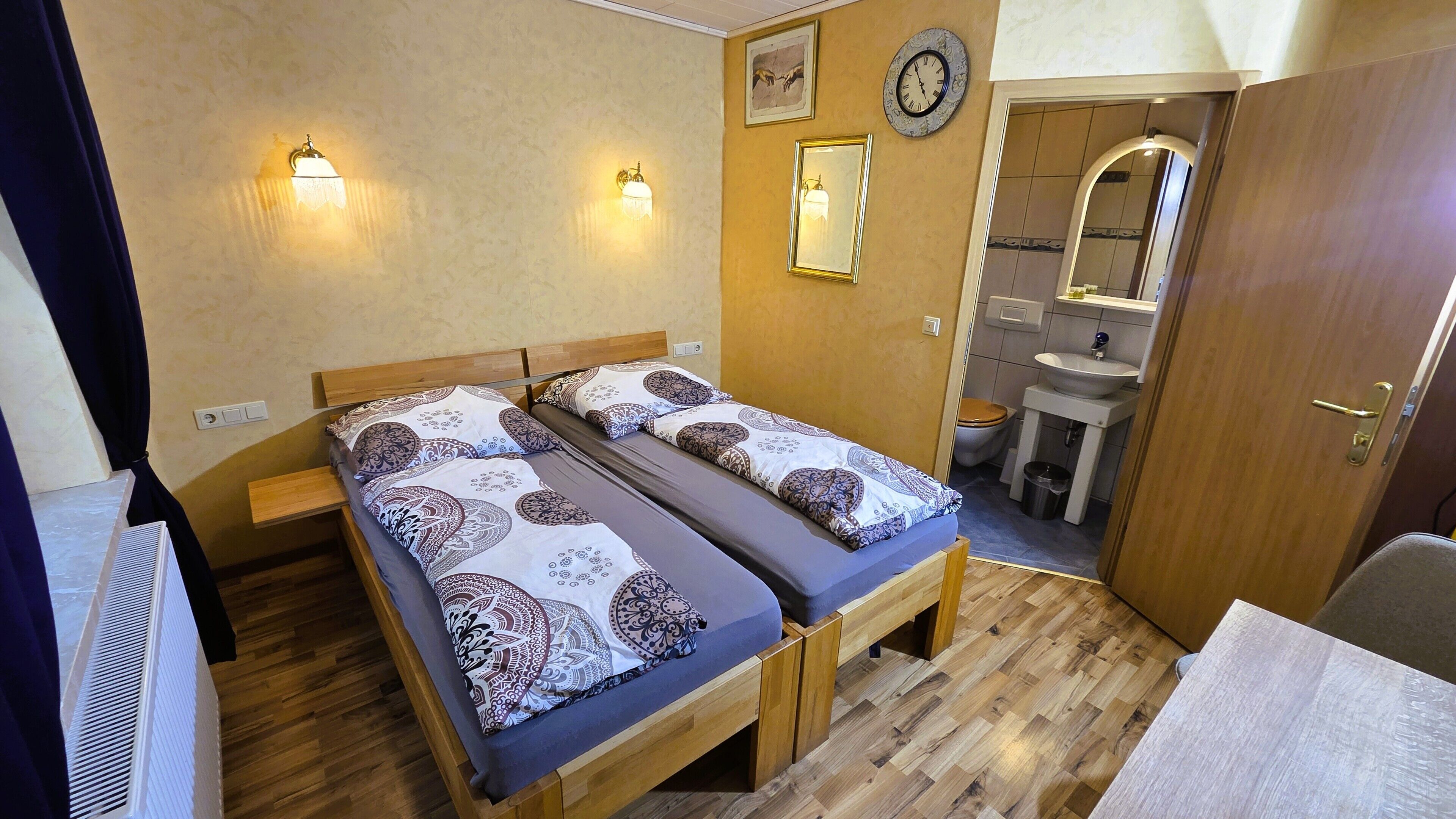 A double room with two beds, a wooden floor, a bathroom with a sink and toilet, and a mirror.
