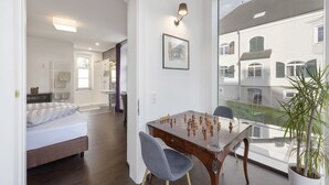 A bedroom with a bed, a bathroom with a shower, and a dining area with a chessboard. - Villa Maria - Suiten & Appartements (Kufstein)