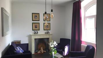 A living room with a fireplace, two armchairs, a coffee table, and a chandelier.