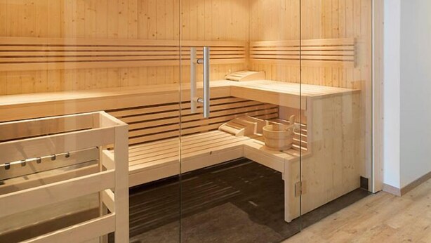 A sauna with wooden walls and benches, a glass partition, and a small table with cups. - Villa Maria - Suiten & Appartements (Kufstein)
