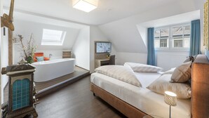 A modern bedroom with a large bed, a desk, a bathtub, and a TV. - Villa Maria - Suiten & Appartements (Kufstein)