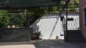 A courtyard with a staircase leading to a building, surrounded by greenery and a white wall. - Apartment Kalin (Piran)