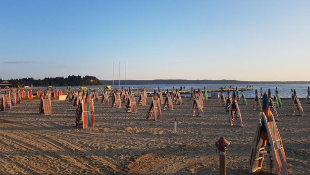 A beach with numerous colorful beach umbrellas and lounge chairs arranged in rows. - Apartment Kalin (Piran)