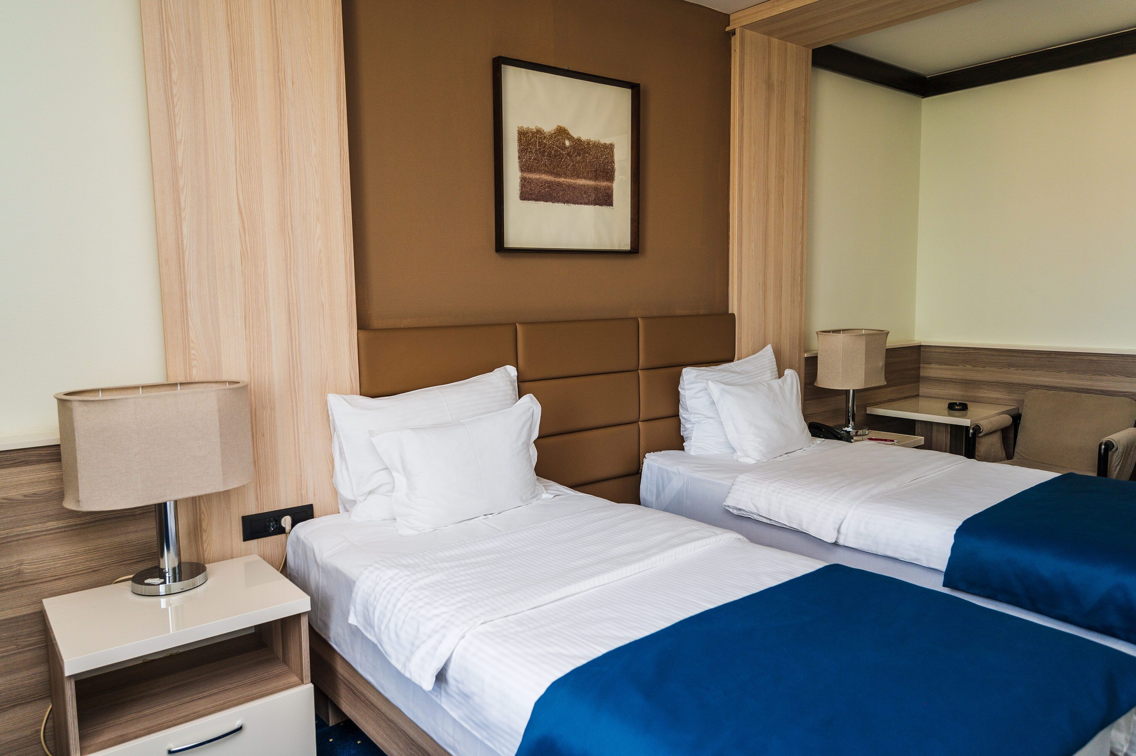 A hotel room with two beds, a nightstand, a lamp, and a framed picture on the wall.